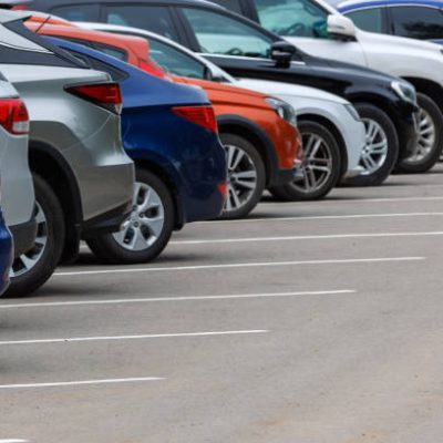 row of different color cars on asphalt parking lot at cloudy summer day with selective focus